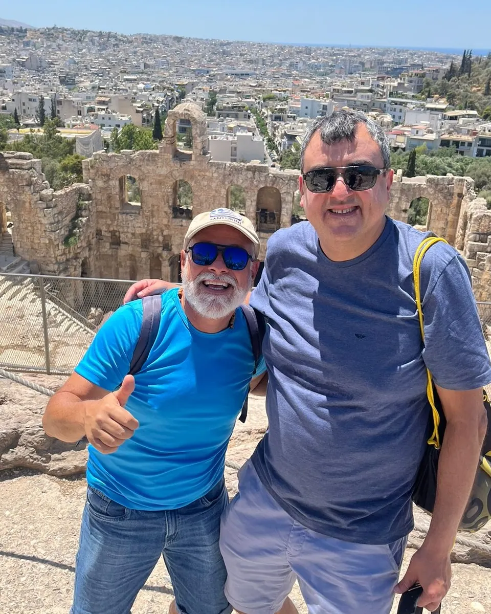 Carlos Adriano com viajante no Odeon de Herodes Ático, com Atenas ao fundo